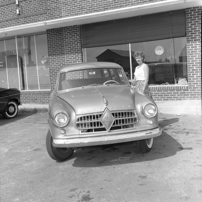 Eine Frau steht neben einem Borgward Auto vor einem Gebäude.
