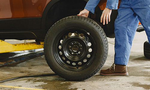 Ein Mann in blauen Overalls steht neben einem Reifen.